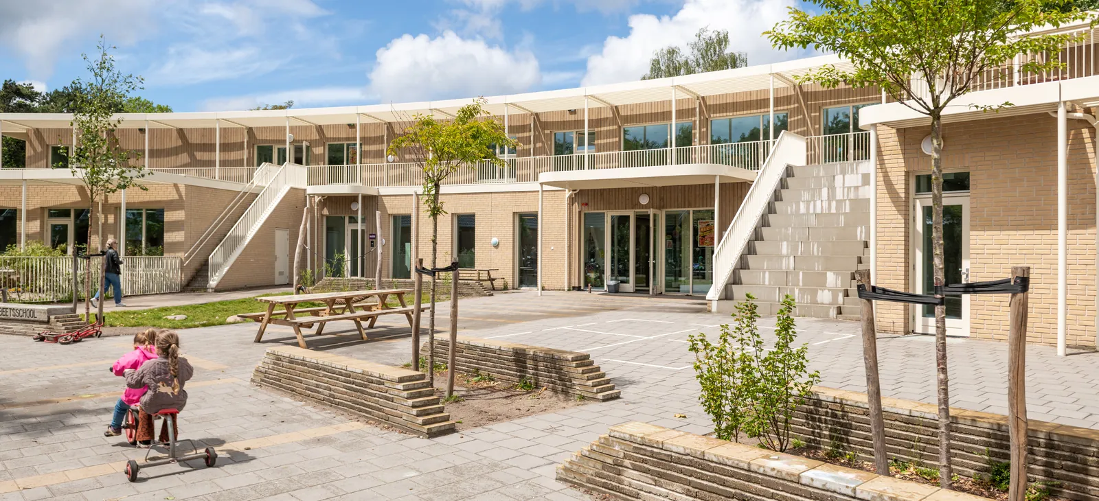 Het binnenplein van de school met trappen naar de bovenverdieping, picknicktafels en jonge bomen