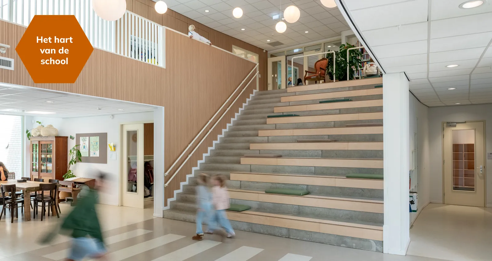 De centrale hal met de brede tribunetrap en bolvormige lampen, met het label Het hart van de school