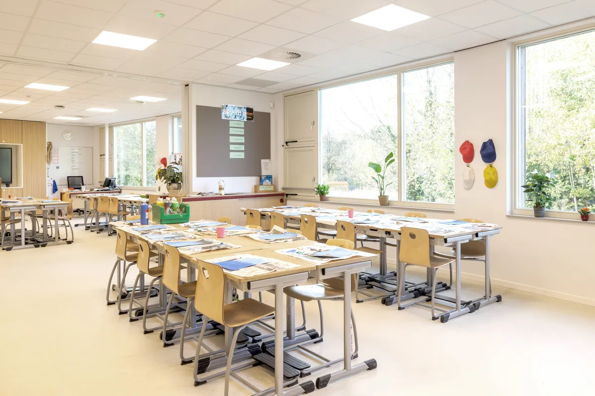 Licht klaslokaal met grote ramen, tafels en een digibord
